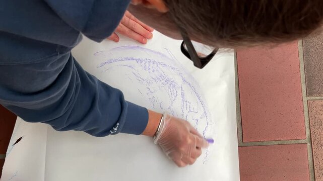 High angle view of woman tracing manhole cover on paper with charcoal