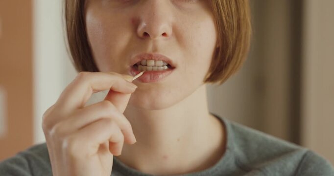 Close-up of a woman using a toothpick to clean her teeth after a meal &mdash; concept of oral hygiene, everyday routine, and dental care.