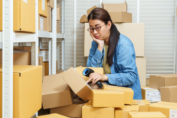 asian woman warehouse worker looking concerned while reorganizing collapsed parcel boxes after stacking accident during ecommerce inventory checking