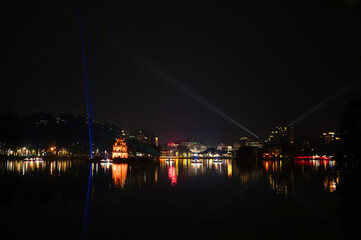 Vietnam, Hanoi - Turtle Tower illuminated at night on Ho&agrave;n Kiếm Lake in Hanoi during a light show, with city buildings visible in the background