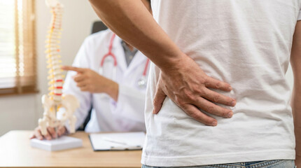 Man with lower back pain consults a doctor explaining spinal health using an anatomical model. Focus on medical diagnosis, treatment, and chiropractic care