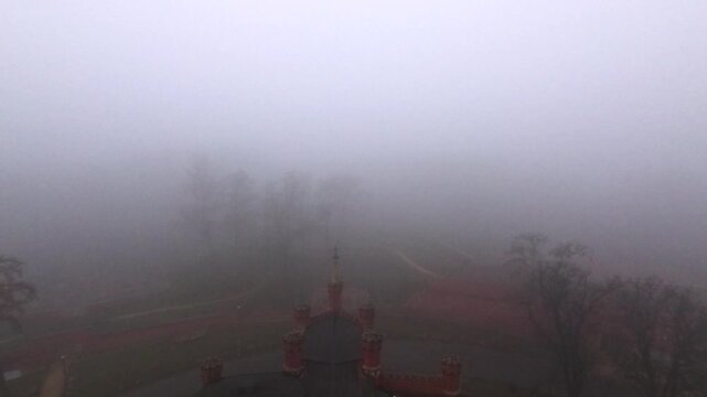Fog blankets a landscape at dawn, making it hard to see far. Shadows of trees and figures appear in the distance, creating an unclear view of the surroundings.