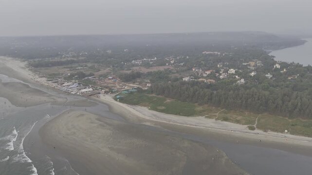 Aerial evening view of Morjim turtle nesting beach, Goa in winter, showing gentle waves, boats along the shore, coconut palms, coastal vegetation, Chapora River, and soft mist creating a calm tropical