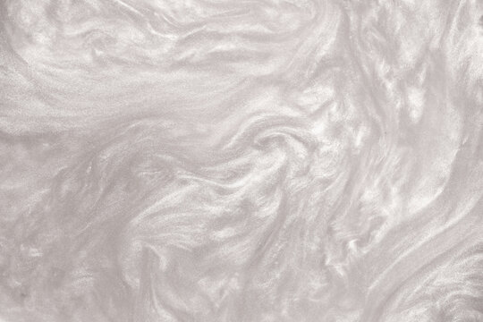 Shimmering silver abstract background. Liquid glitter paint texture waves and swirls. Beautiful shiny white glitter texture. Metallic silver paint close-up as a holiday background.