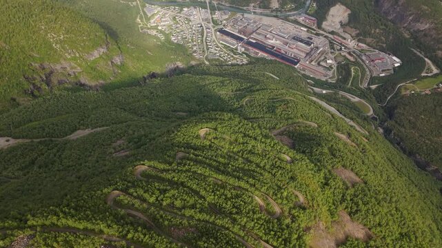 A Winding Bicycle Route Cuts Across a Lush Mountainside Overlooking an Industrial Valley Along Tusenmeteren in &Oslash;vre &Aring;rdal, Norway - Bird's Eye View Shot