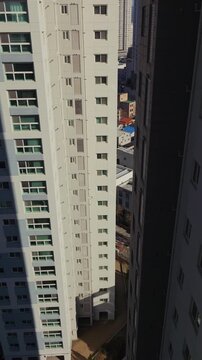 Vertical shot tilting up revealing facade of multi story residential apartment complex against clear blue sky in Daegu city urban area