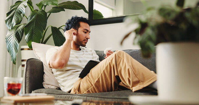 Man, relax and earphones with tablet in living room for movie, streaming film or listen to audio. Person, home and digital tech for social media, online podcast and sound for music entertainment