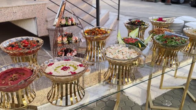 Elegant outdoor catering table with Arabic mezze dips, fresh salads and shrimp canap&eacute;s on gold stands&mdash;ideal for weddings, corporate events, Ramadan iftar and banquets.