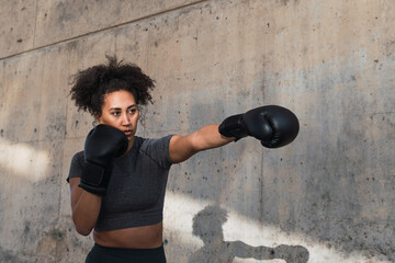 Young woman wearing boxing gloves practicing her punches against a concrete wall