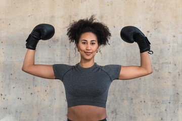 Confident sportswoman wearing boxing gloves is flexing her biceps