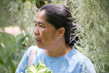 Woman stands amidst green foliage in a garden while observing the surroundings during a sunny day