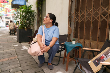 Older woman rests on chair in urban area with colorful decorations during daytime