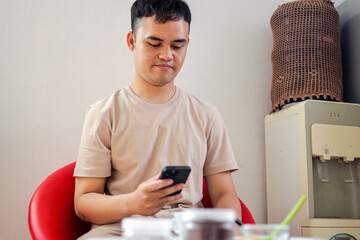 Young Man Sitting at Table Focused on Smartphone in Casual Setting