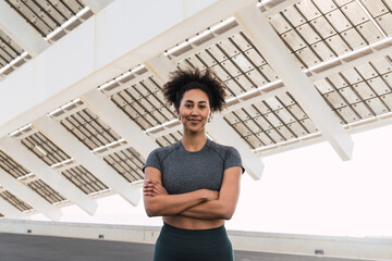 Sportswoman posing with crossed arms and smiling under a futuristic white metal structure