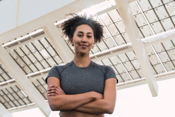 Smiling athlete standing with crossed arms under a large solar panel roof