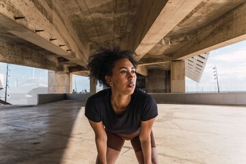 Athletic young woman pausing under a bridge during her outdoor run