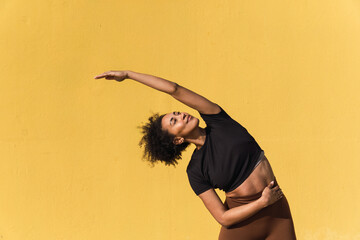 Fit woman practicing yoga against a vibrant yellow wall, promoting a healthy and active lifestyle