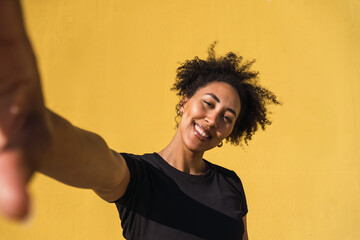 Smiling young woman taking a selfie against a vibrant yellow wall