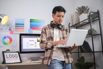 Designer Working on Laptop in His Modern Office, Surrounded by Logo Design Assets and Color Charts
