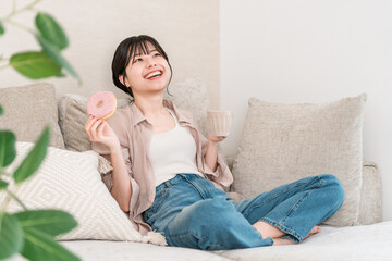 Young Asian woman sitting on a sofa in the living room and eating a donut