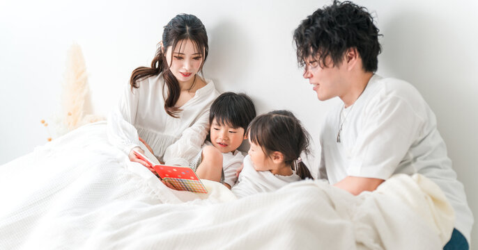 Mother and father reading a picture book to their child in bed (putting to sleep, taking a nap, reading aloud)
