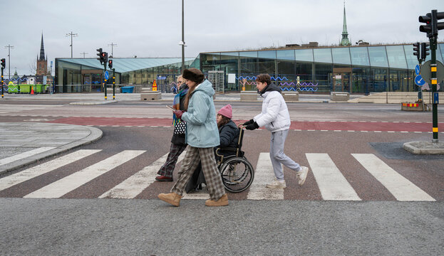 Family crossing street in Stockholm during winter while supporting wheelchair user, showcasing accessibility and inclusion in modern urban environment