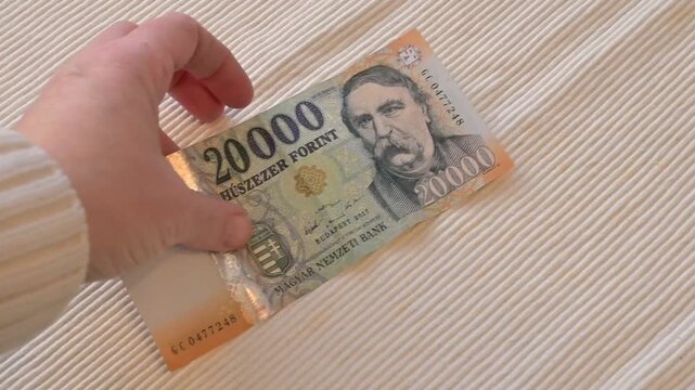 Close-up video of a female hand taking a twenty thousand Hungarian forint banknote from a table on a white background with Copy Space. Financial concept illustrating spending, payment, loss.