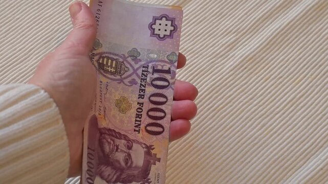 Close-up video of a female hand taking a ten thousand Hungarian forint banknote from a table on a white background with Copy Space. Financial concept illustrating spending, payment, loss, cost of life