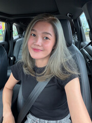 Asian Thai woman with ash-blonde hair smiling and  take selfie while sitting in car, happy traveling alone.