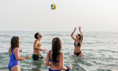 Young friends playing volleyball in ocean having fun