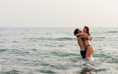Happy young couple embracing in ocean water enjoying summer vacation