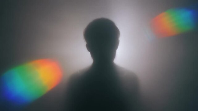 Silhouette of a person surrounded by rainbow lights and fog.