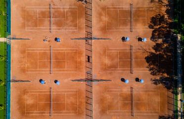 Top-down aerial view of clay tennis courts separated by a walkway with umbrellas and seating. Clean geometric layout, symmetry, warm colors, outdoor sports and recreation concept