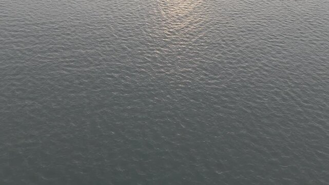 Top-down aerial close-up of the Arabian Sea near Mobor Beach, Goa, capturing shimmering ocean water with bright sun reflection creating a sparkling texture and tranquil coastal mood.