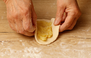 A person is making a pastry with a filling of mashed potatoes