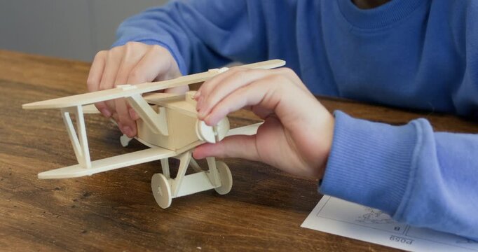 Little boy hands press wooden airplane details sitting at desk closeup. Schoolboy works on toy biplane model made of plywood material at home. Learning engineering
