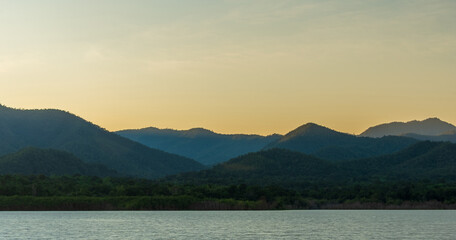 Golden hour light over mountain range with warm sky and calm lake.