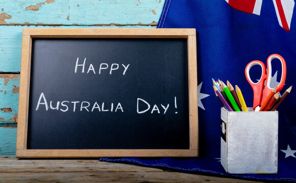 Writing slate with happy australia day text by desk organizer on flag over table