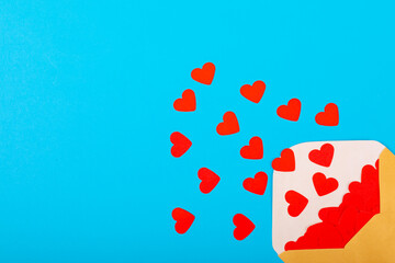 Open beige envelope with red heart shapes by copy space on blue background