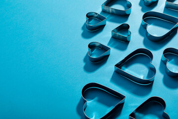 High angle view of heart shape pastry cutters with shadows by copy space on blue background