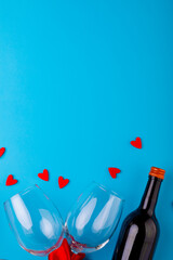 Red heart shapes by wine bottle and empty wineglasses over blue background with copy space