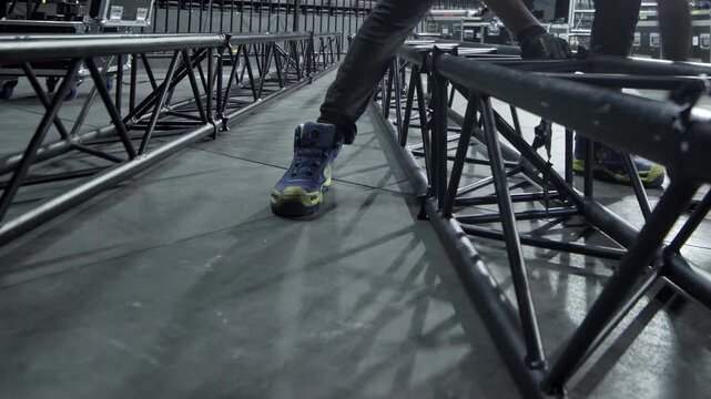 Worker places screws assembling beam frames columns on stage closeup. Employee uses bolts to fasten metal carcass for concert show