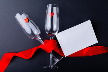Empty champagne flutes tied with red ribbon by envelope with copy space over gray background