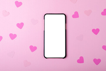Overhead view of smart phone with copy space and heart shaped decoration on pink background