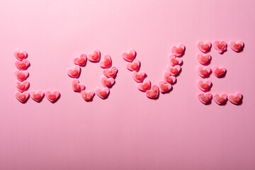 Love text made from heart shaped candies isolated on pink background, copy space