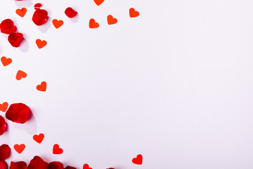 Naklejka premium Overhead view of red heart shaped decoration and rose petals with copy space over white background