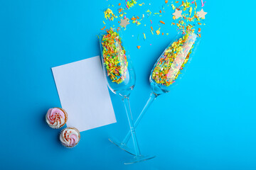 Overhead view of cupcakes and champagne flutes with confetti on blue background, copy space