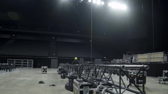 Worker checks beam with powerful lamps before lifting on stage. Employee works with lighting on support equipment in modern concert hall