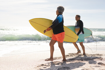 Obraz premium Side view of multiracial senior couple walking with surfboards on sunny beach