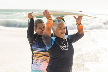Obraz premium Happy multiracial senior couple carrying surfboard on heads against sea at beach during sunny day